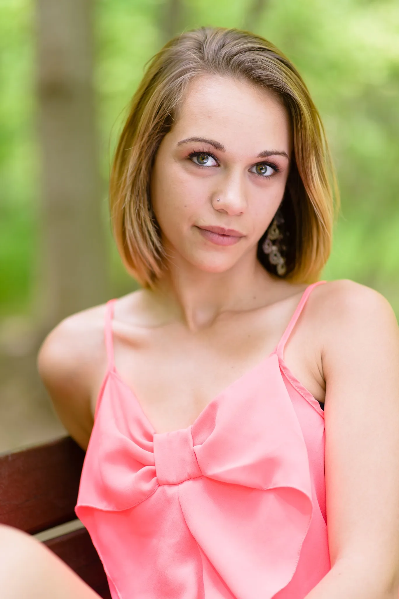 Aliyah on a bench in a coral top with a large bow, her head tilted toward the camera