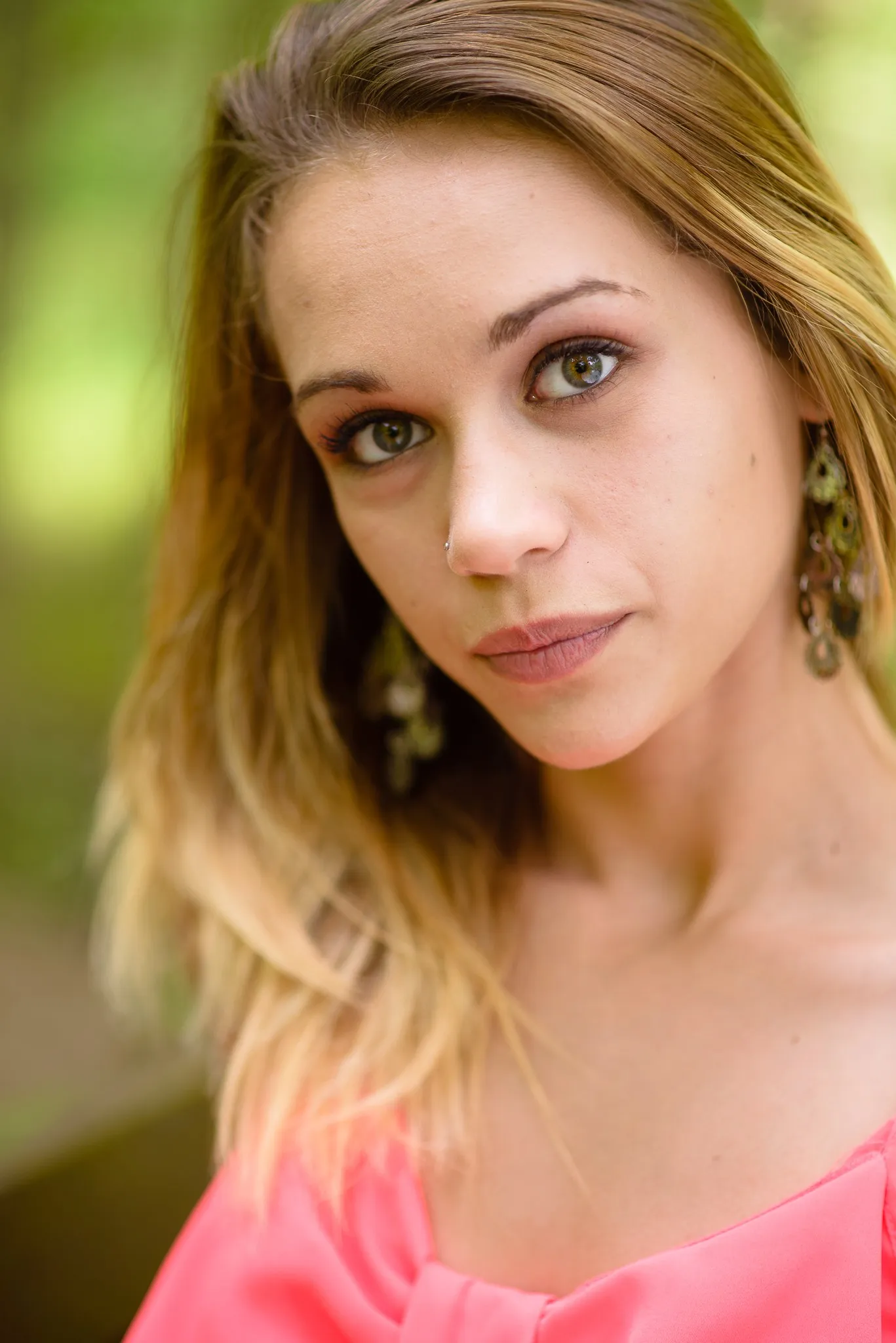 Close portrait of Aliyah in long drop earrings, sunlight in her hair and green woods soft behind her