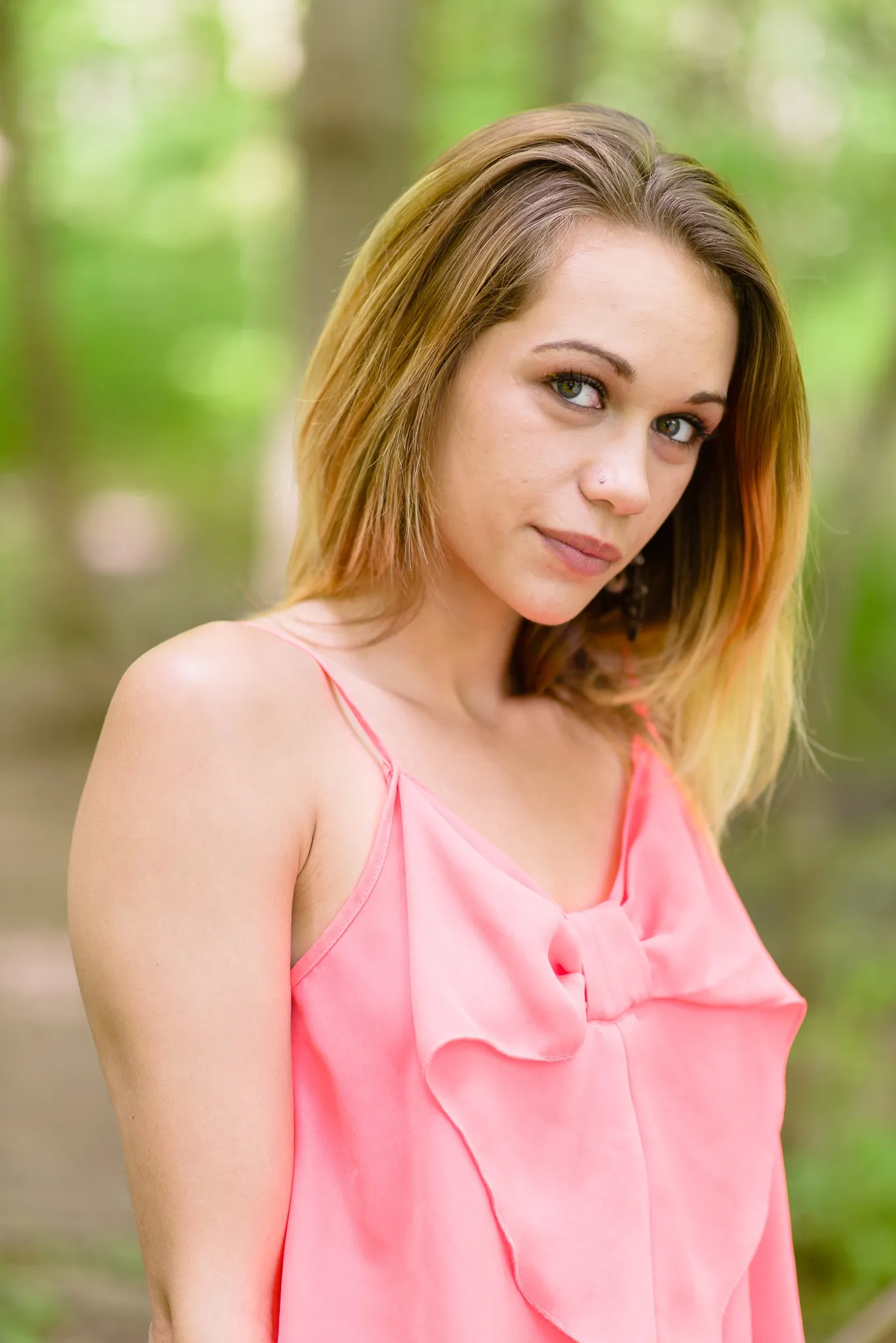 Aliyah looking over her shoulder in a coral camisole, the trees blurred behind her