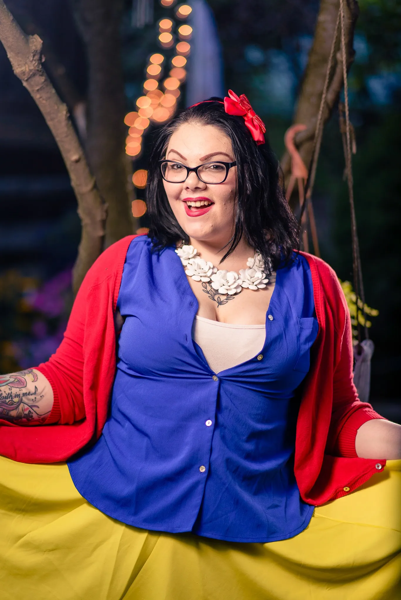 Carly laughing and holding out her yellow skirt, string lights glowing in the trees behind her
