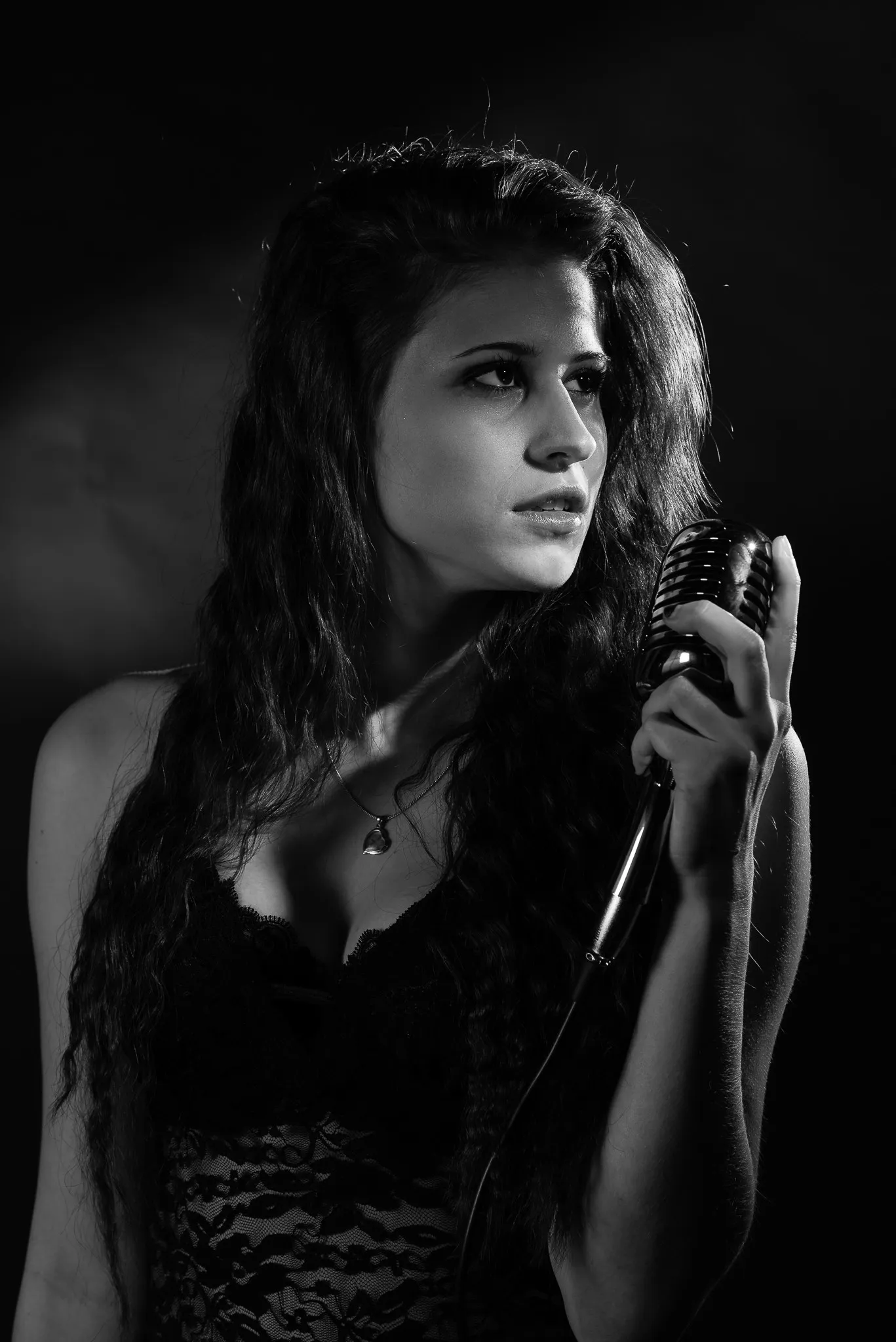 Black and white: Kat in a black lace dress holding a vintage microphone, looking away