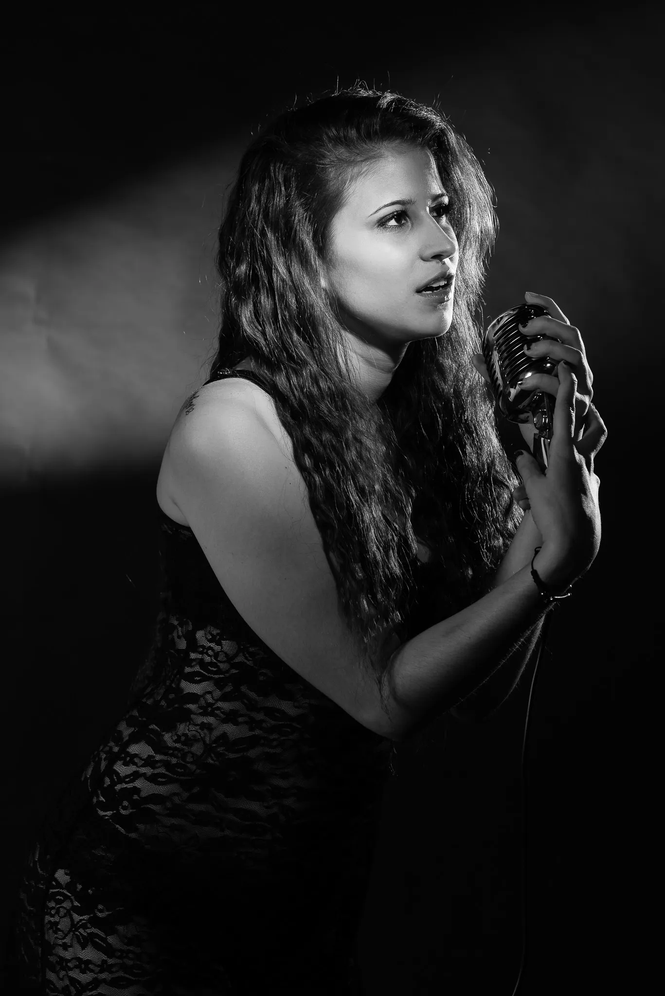 Black and white: Kat leaning into a vintage microphone in a spotlight
