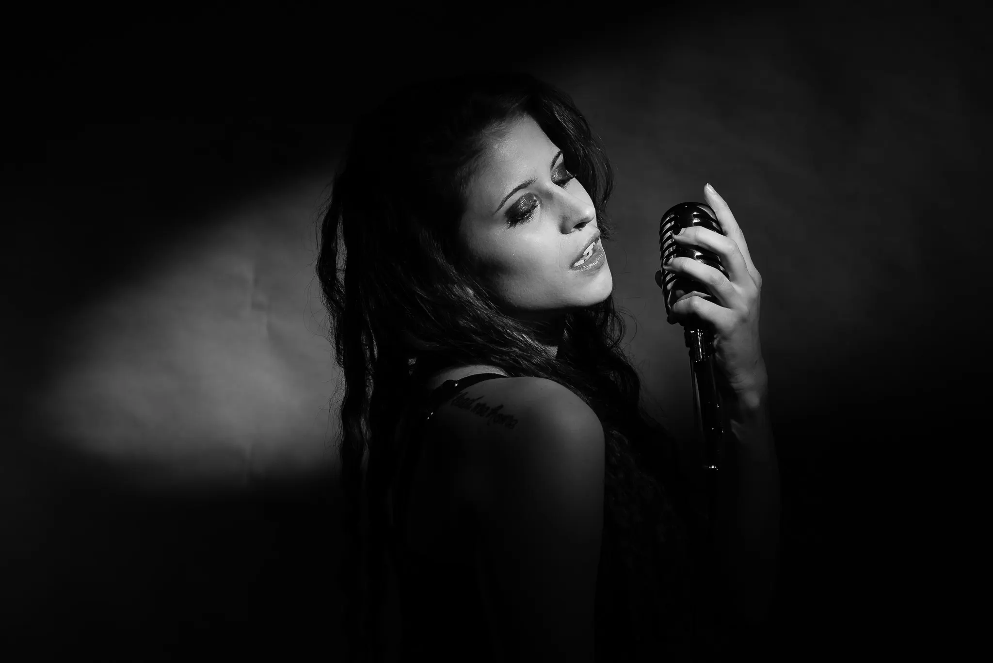 Black and white: Kat singing into a vintage microphone at the edge of a pool of light