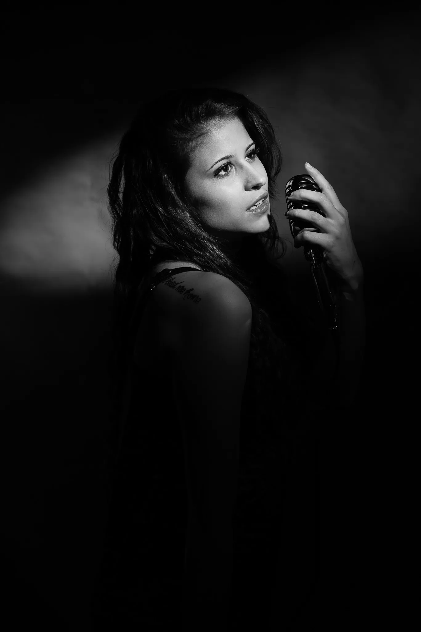 Black and white: Kat at a vintage microphone, looking over her shoulder, half in shadow