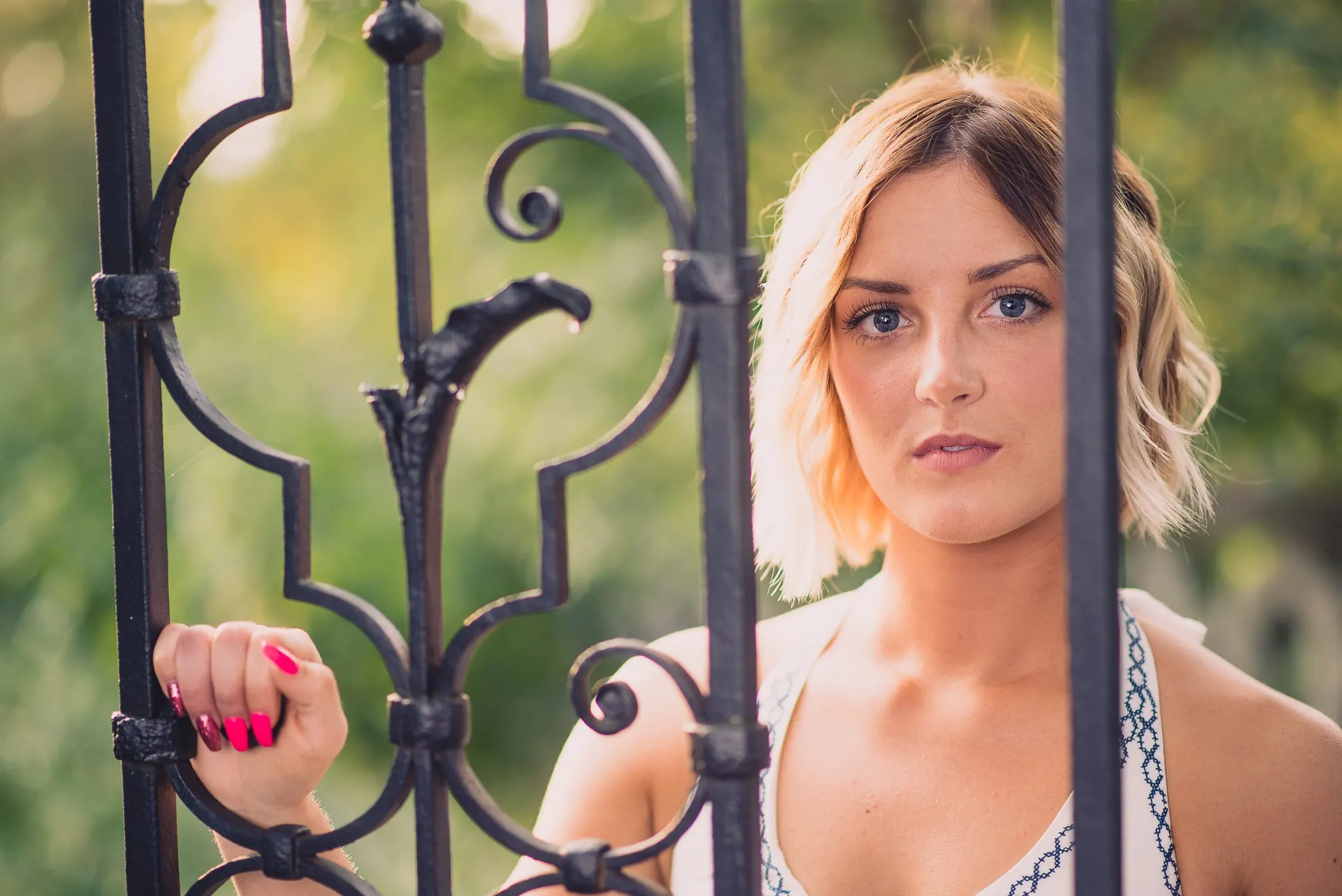 Sam looking through the bars of an ornate wrought-iron gate, one hand on the scrollwork