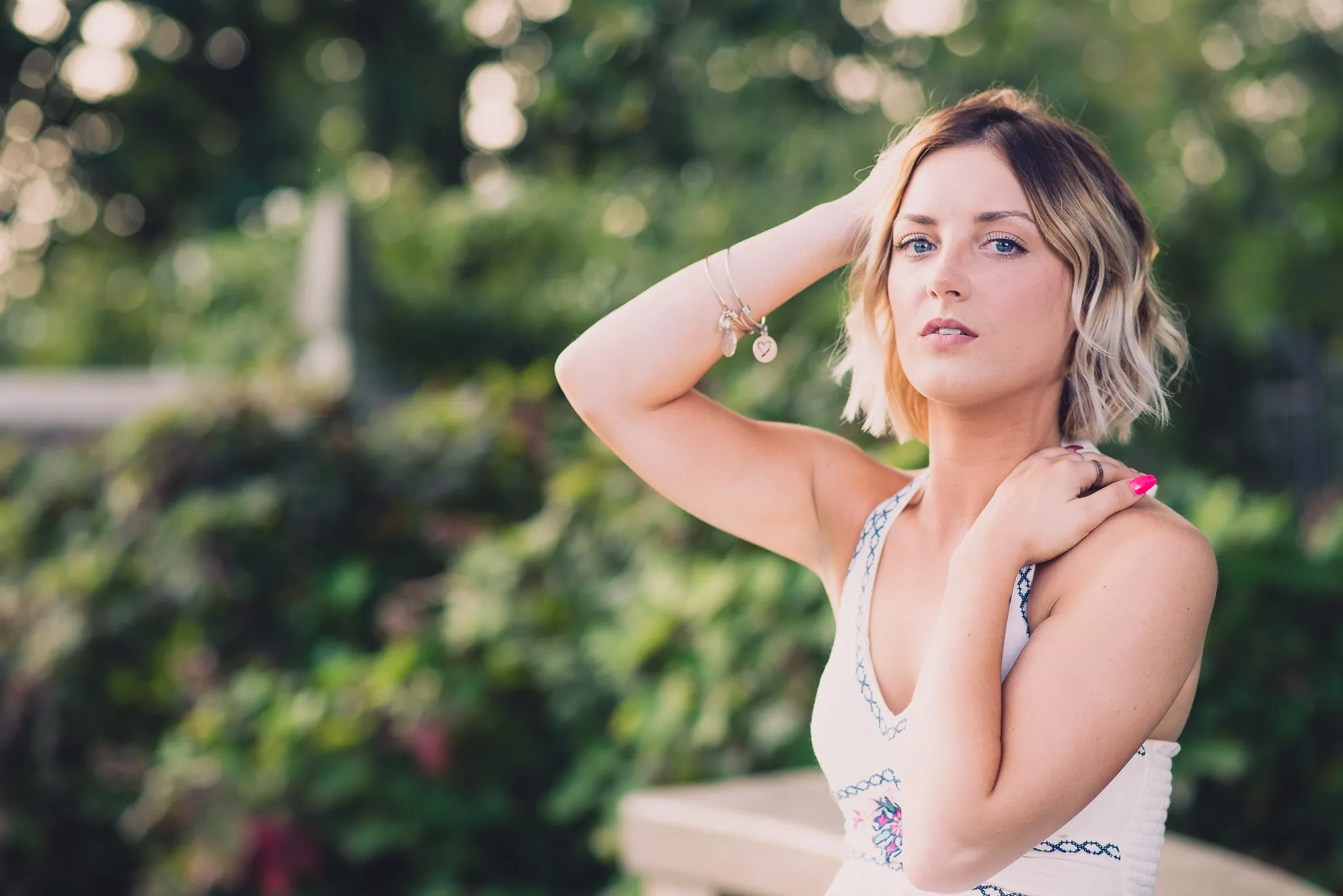 Sam with one hand behind her head and the other on her shoulder, a garden soft behind her